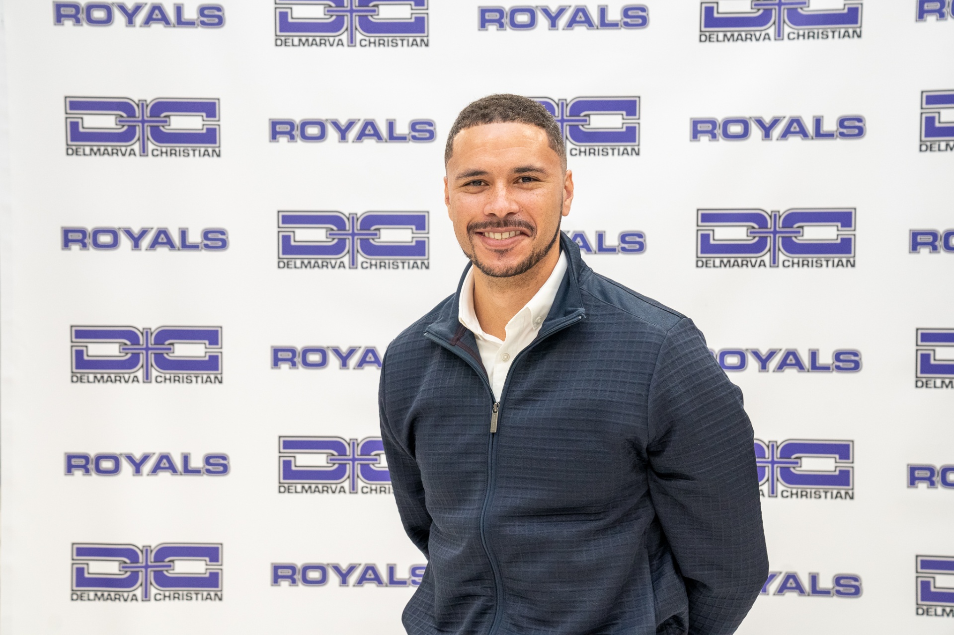 Toné King smiling in a navy quarter-zip jacket.
